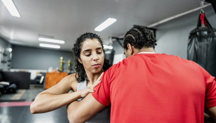 Mulher com cabelo cacheado treinando tÃ©cnica de autodefesa ou luta com homem em camisa vermelh...
