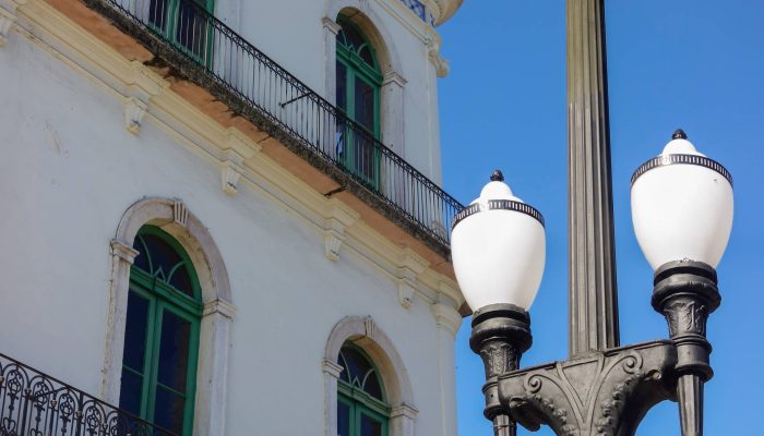 Fachada branca de edifÃ­cio histÃ³rico com janelas verdes arqueadas e varandas de ferro forja...