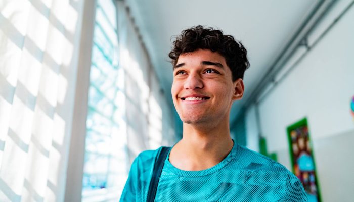 Jovem feliz com cabelo encaracolado sorrindo em corredor iluminado por janelas